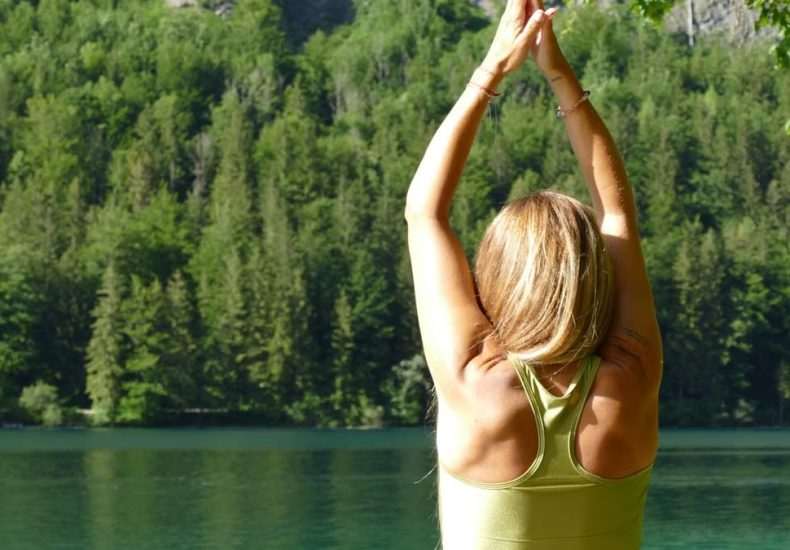Back view of a woman meditating in a yoga pose by a serene lake in Ebensee, Austria.