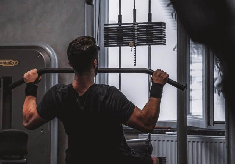 Back view of a man exercising with lat pulldown machine in the gym.